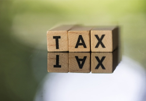 "TAX" branding with a money bag icon and wooden blocks reflecting on a surface.